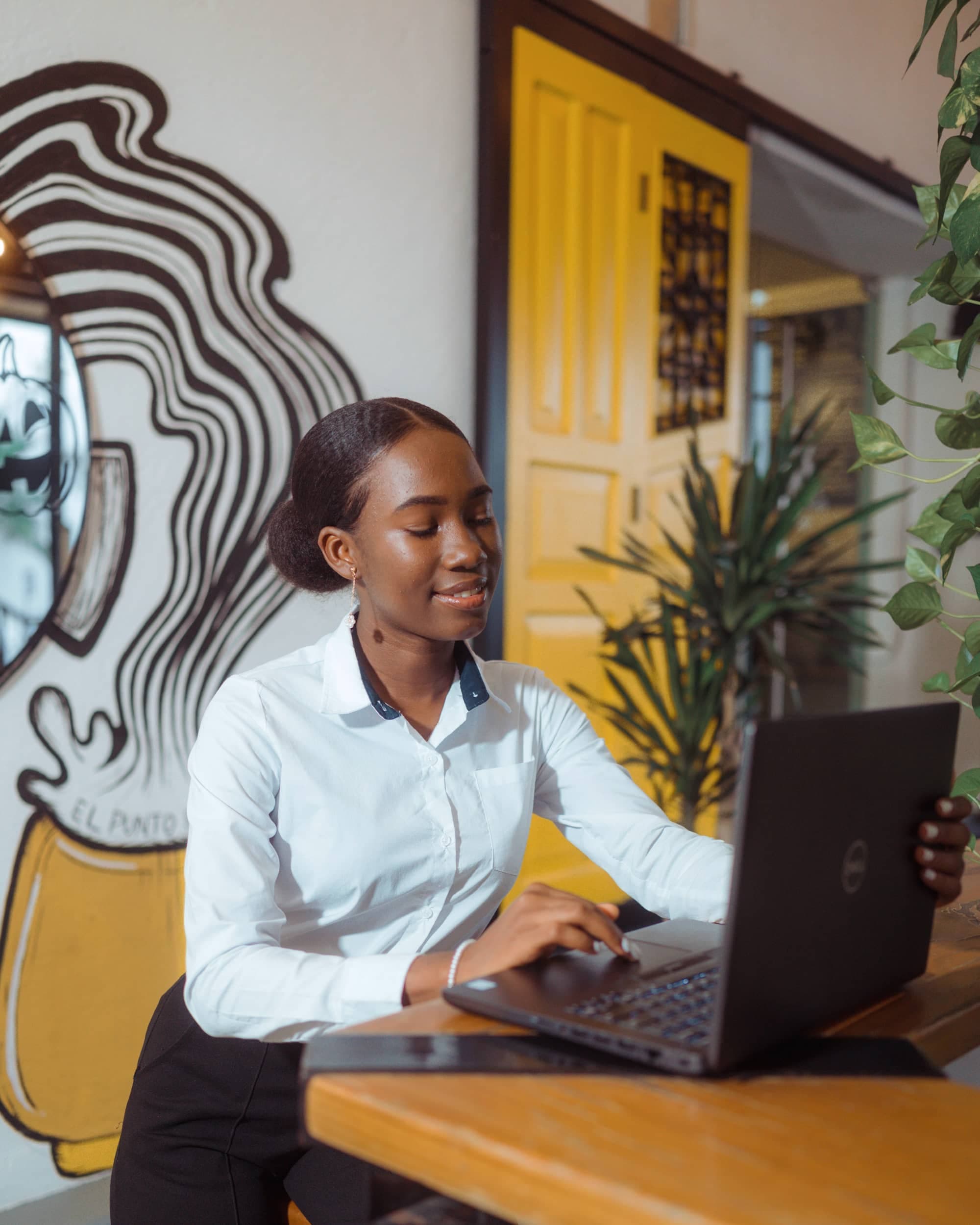 A young professional in a white shirt smiling while working on a laptop at a café table
