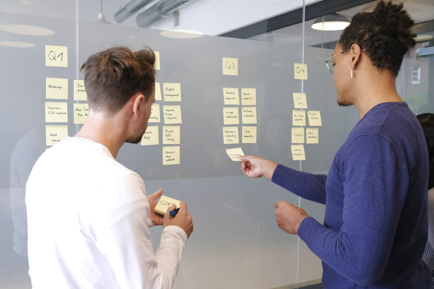 Two colleagues arranging sticky notes on a glass wall during a planning session