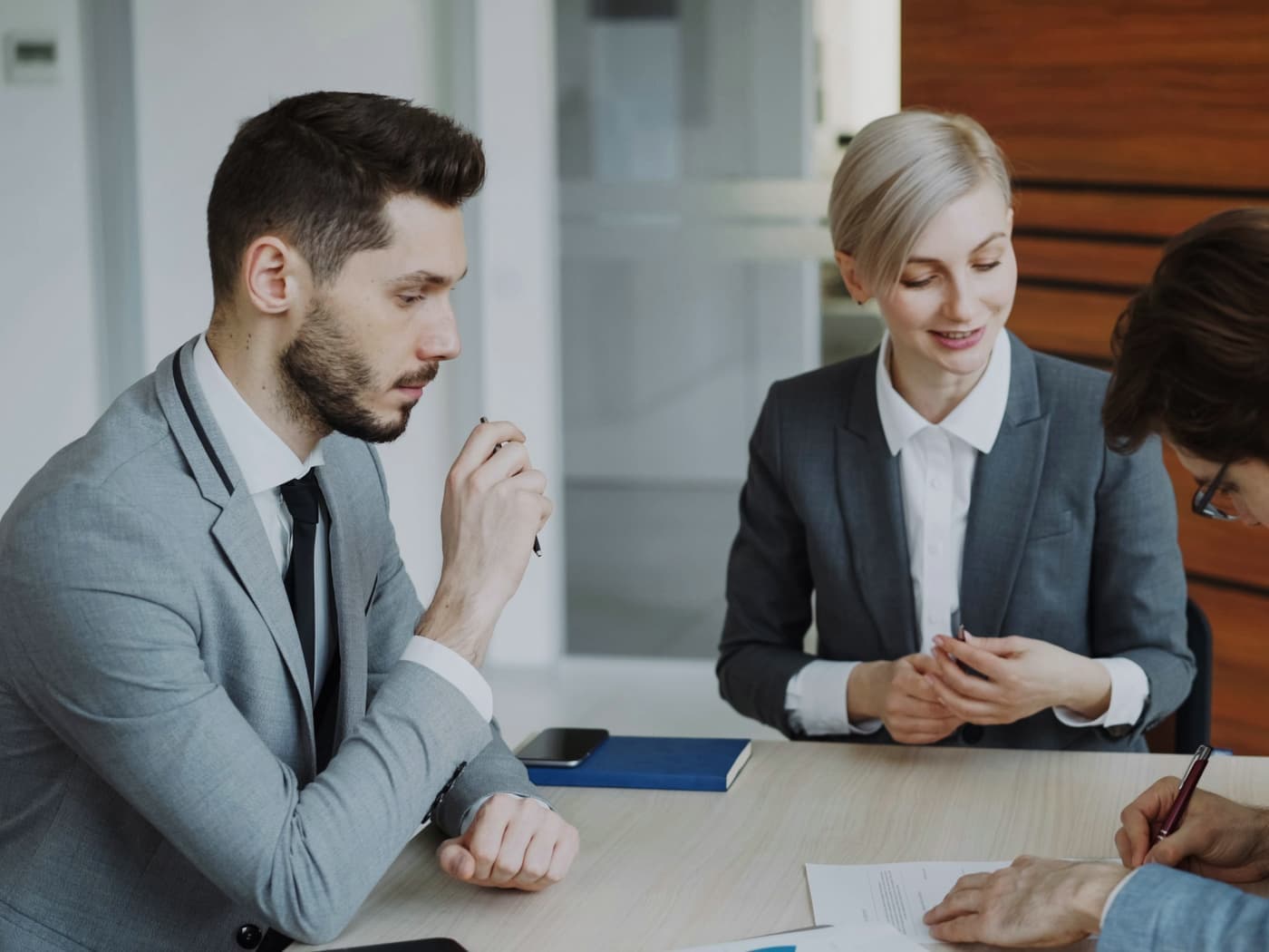 Three professionals in suits reviewing a document at a meeting table
